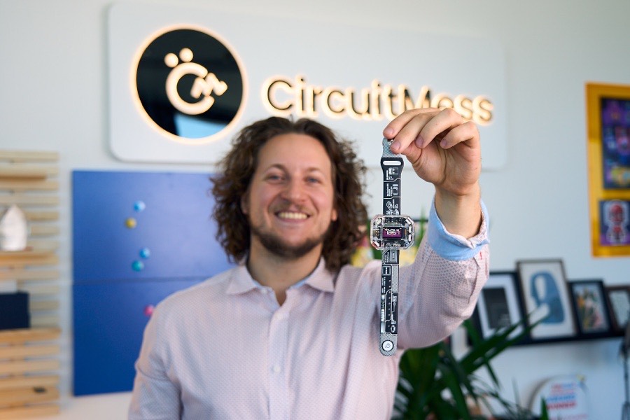 Albert Gajšak holding up a buildable smartwatch by its strap, CircuitMess logo behind him.