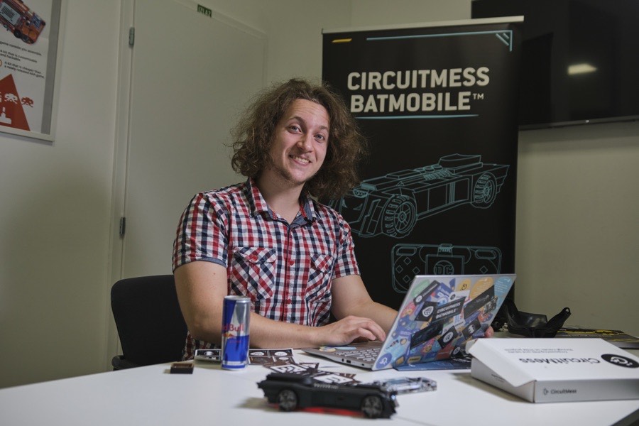 Albert Gajšak working at a laptop in front of a large CircuitMess Batmobile banner, with the model car on the desk.
