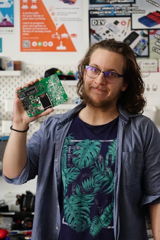 Albert Gajšak in the workshop, holding up a bare green circuit board.