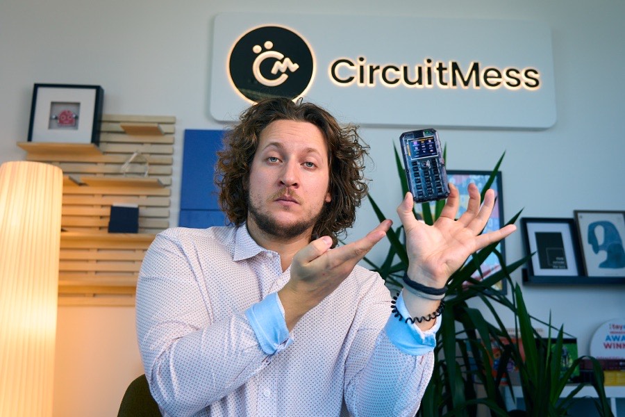 Albert Gajšak gesturing with both hands towards a MAKERphone floating in mid-air, CircuitMess logo behind him.