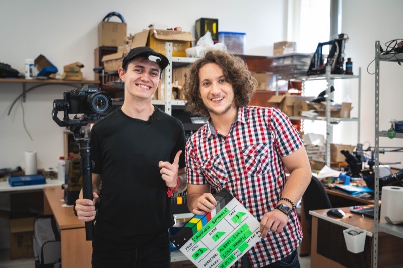 Albert Gajšak holding a film clapperboard next to a colleague with a camera rig, in the CircuitMess workshop.